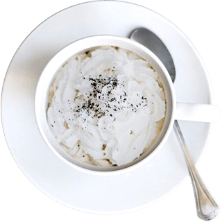 White coffee cup with whipped cream and chocolate sprinkles on a saucer, accompanied by a spoon.