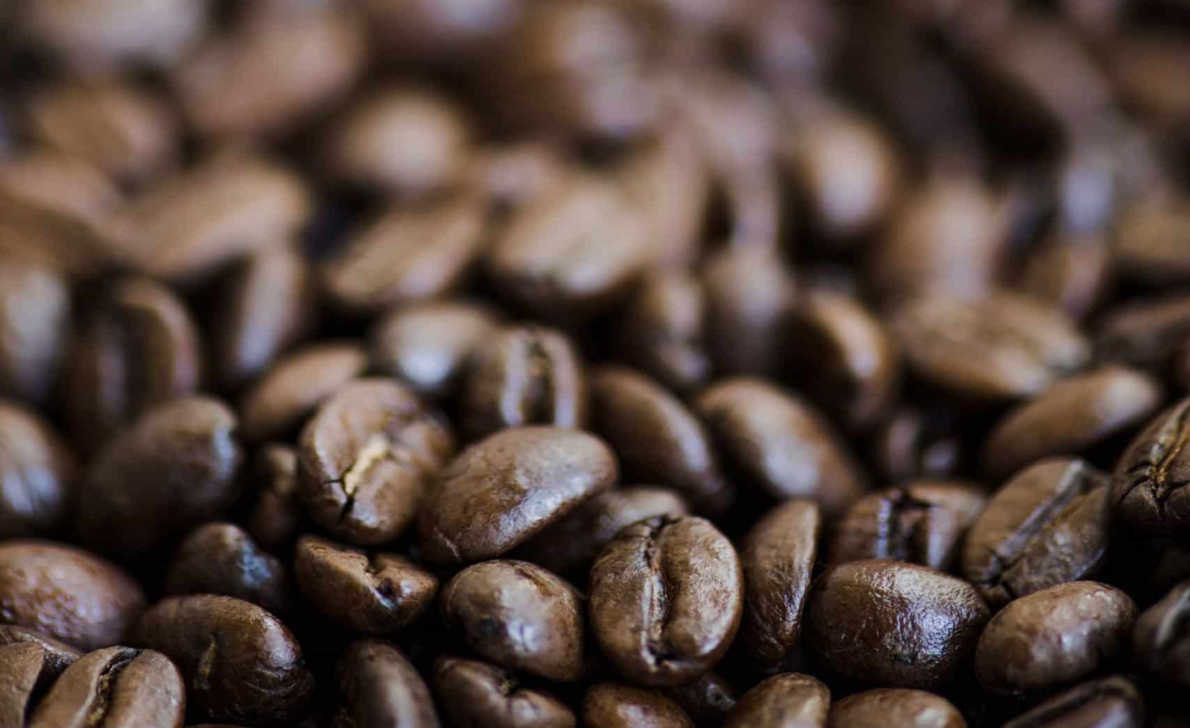 Close-up of roasted coffee beans with glossy, textured surfaces in different shades of brown.