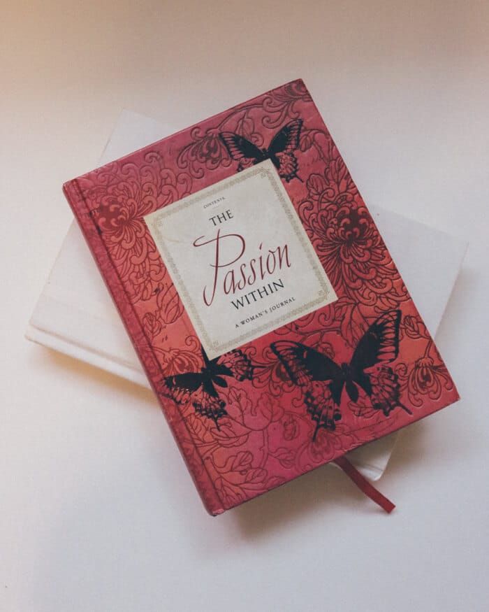 divi-girl-book A red hardcover book titled The Passion Within with butterfly and floral designs sits atop a plain white book.
